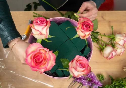 Pink roses in floral foam inside a round container on a worktable with other flowers around it
