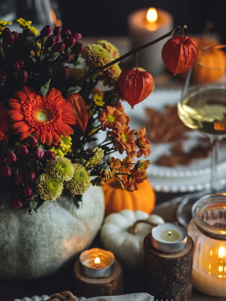 Autumn floral centerpiece with orange gerbera daisies, green mums, berries, Chinese lantern pods, pumpkins, candles, and warm seasonal table d&eacute;cor