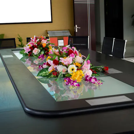 Colorful floral arrangements with lilies, roses, orchids, and gerbera daisies decorating a conference room table