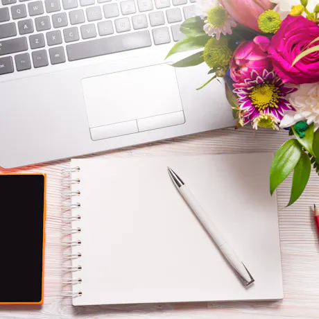 Laptop, notebook, pen, and colorful fresh flowers arranged on a clean workspace