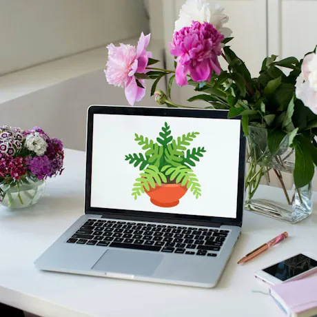 Laptop displaying a plant graphic beside fresh pink peonies and purple flowers in a bright workspace