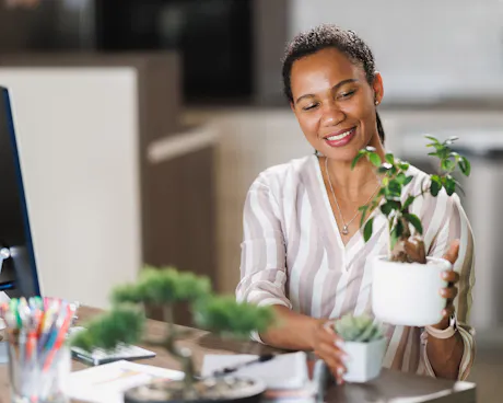 Office worker arranging small potted plants at her desk beside a computer