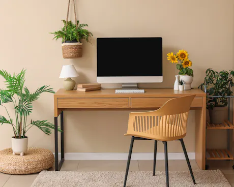 Modern home office with computer, sunflower arrangement, hanging fern, and assorted green houseplants
