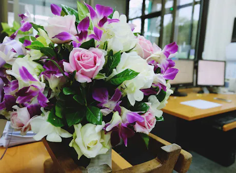 Office flower arrangement with pink roses, purple orchids, white hydrangeas, and greenery beside a workstation