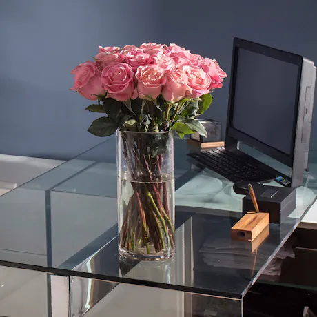 Pink roses in a clear glass vase displayed on a modern office desk beside a computer