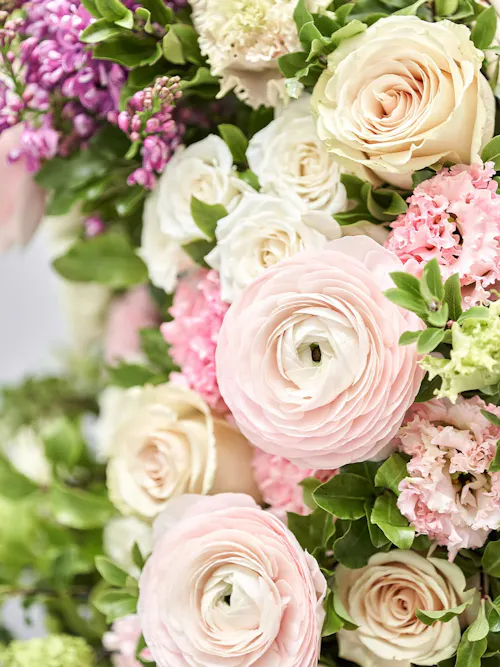 Soft blush ranunculus and ivory roses in a spring floral arrangement