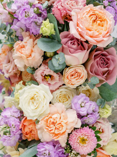 Close up of pink ranunculus, cream roses, and green foliage in a spring bouquet