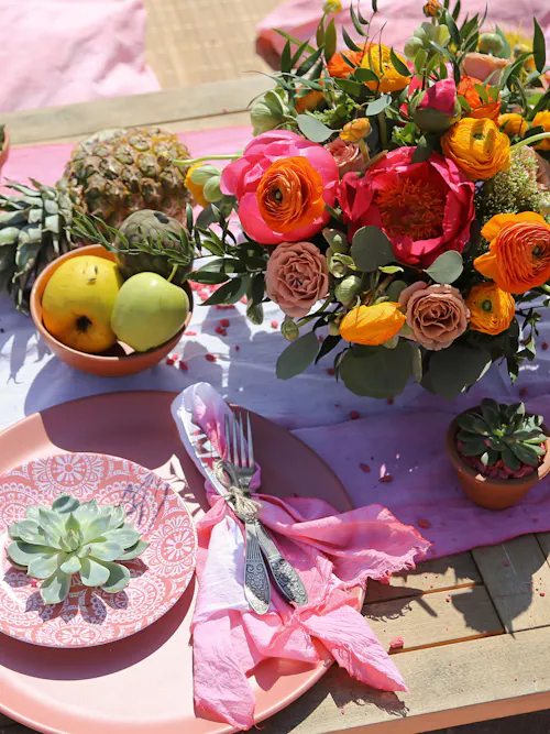 Summer table setting with pink and orange bouquet, fruit, succulents, and pink plates on a wooden table