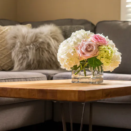 Compact floral arrangement of white hydrangeas and pink roses in a clear glass vase on a coffee table.