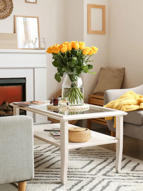 Bouquet of bright yellow roses in a clear glass vase displayed on a coffee table in a warm living room.
